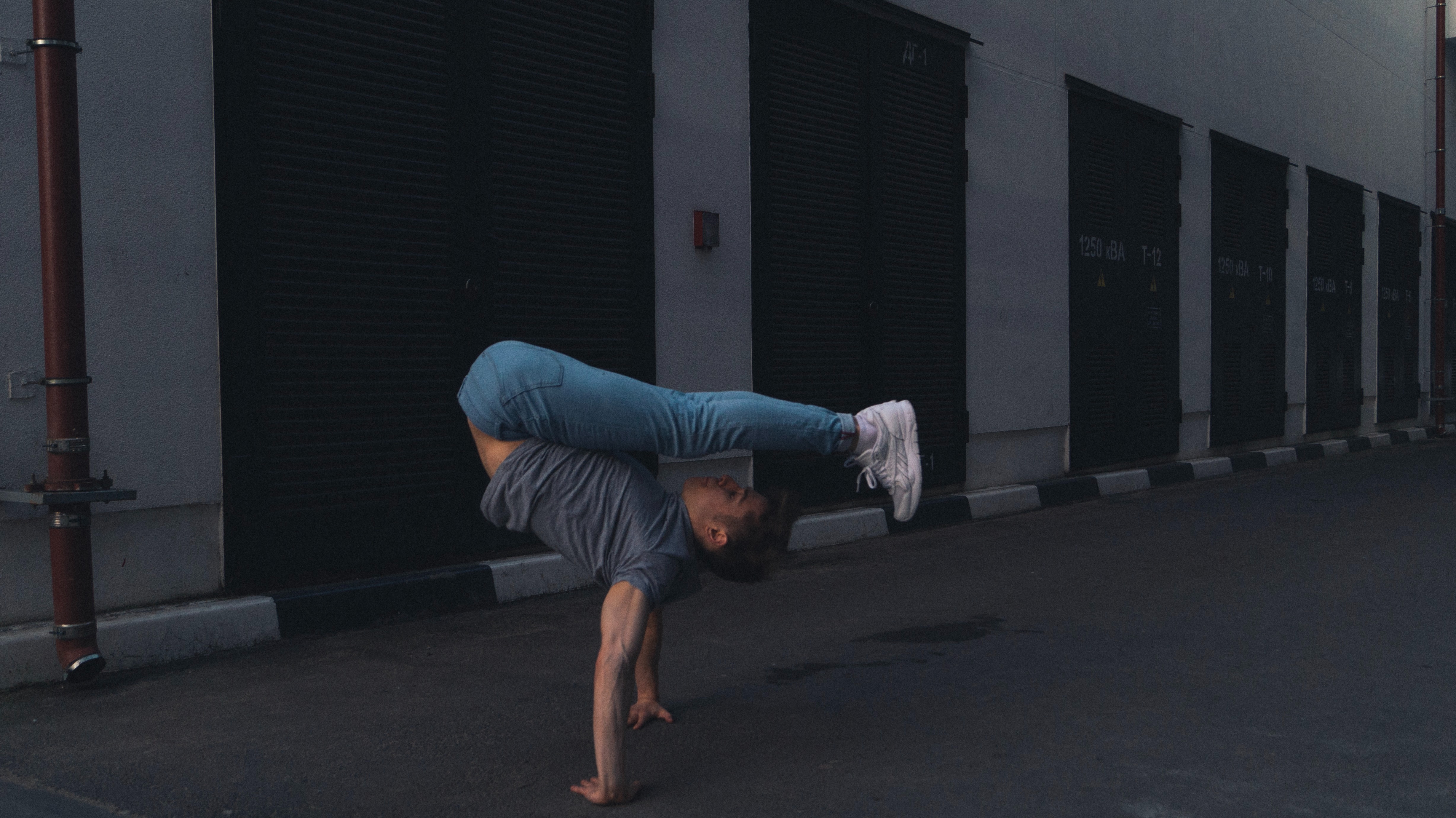 A young man doing a handstand, but his head and feet are pointing in the same direction, perpendicular to his arms.