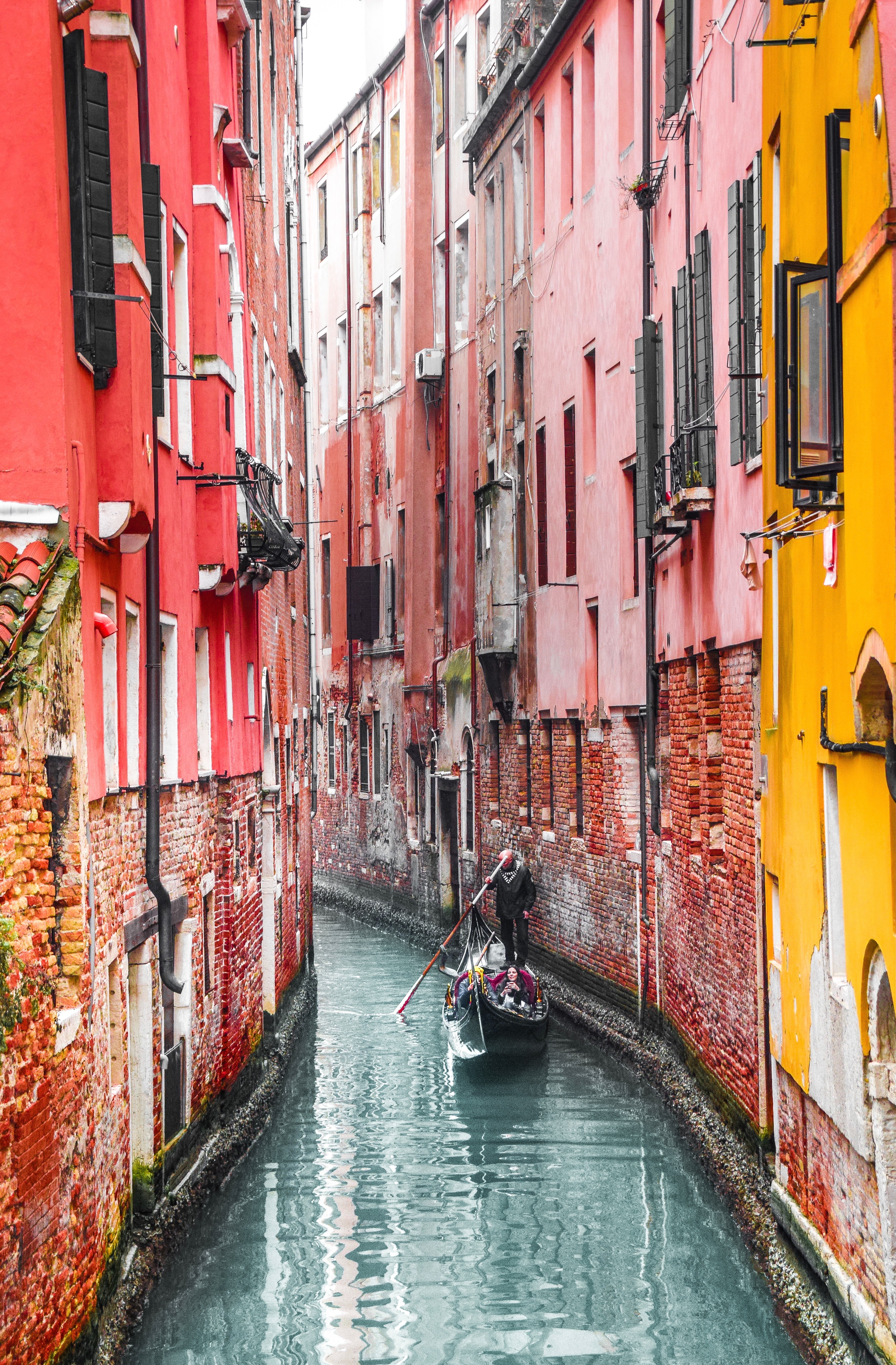 A narrow canal, known as a backstreet, in Venice, with tall, brightly painted buildings on either side.