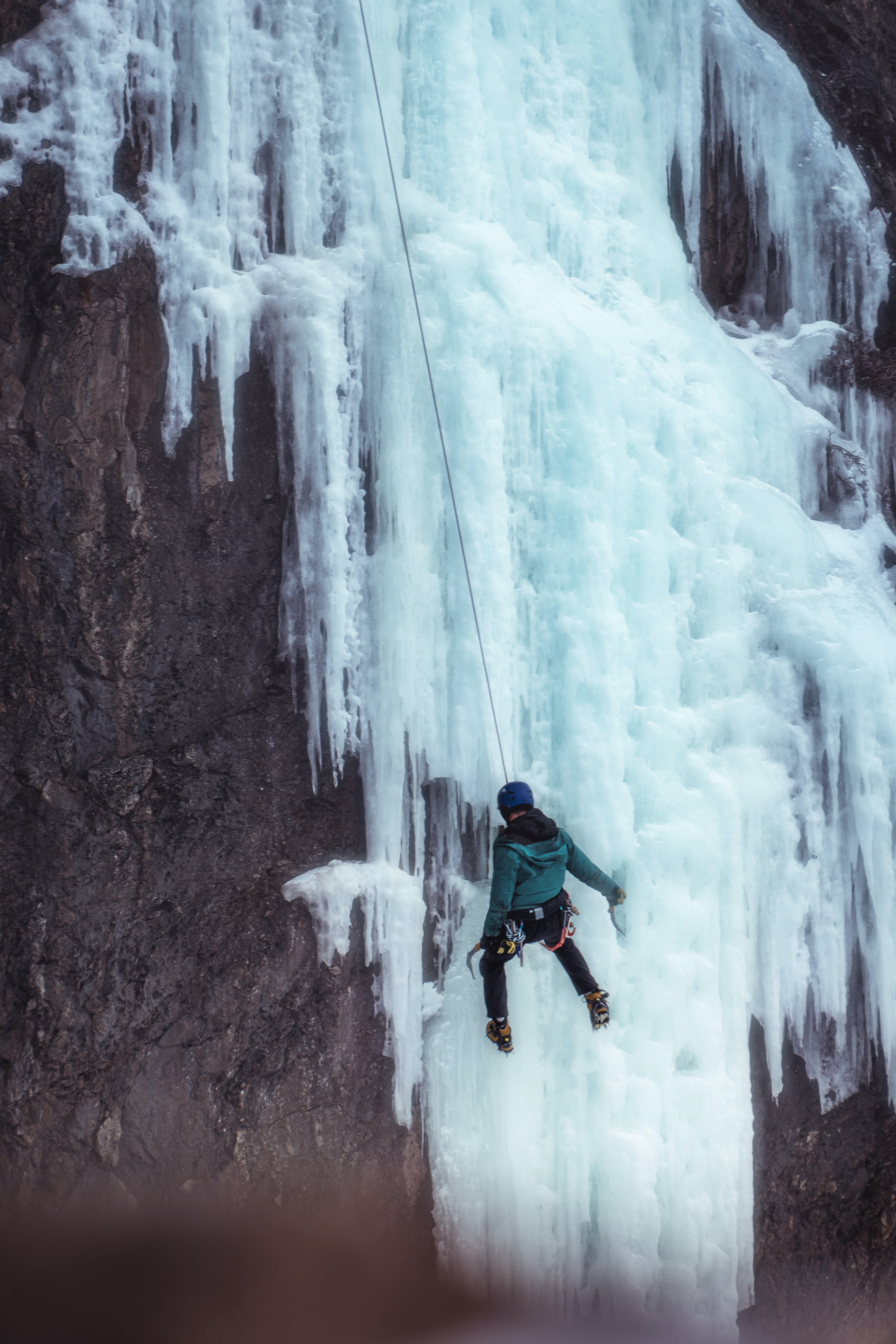 A person with winter clothing and climbing gear who is climbing a frozen waterfall.